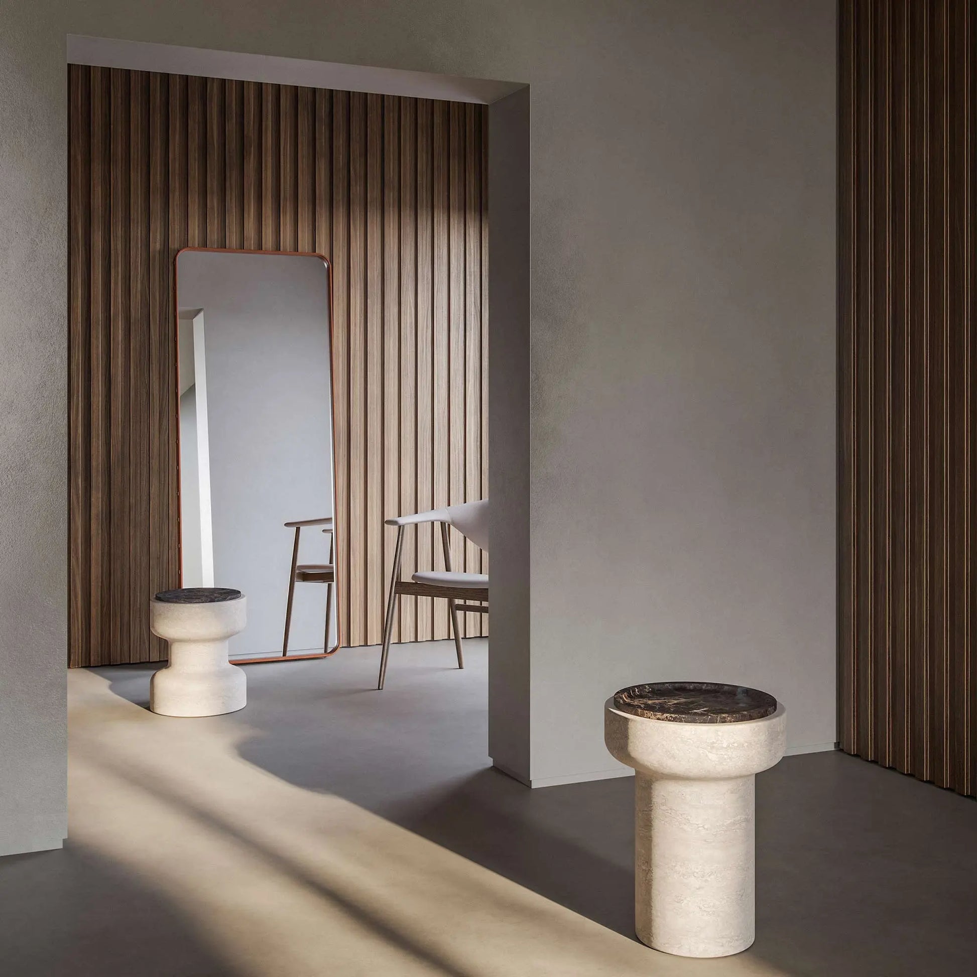 In the foreground, a Tivoli table with Black Emperador top. Doorway behind is a room with Tivoli stool in Travertino Navona base and Black Emperador. A mirror and a chair with wood paneled wall in background. 