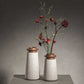 Two Tivoli vases in Travertino Navona marble with Walnut wood top. Large size (left) and Small size (right) with gray background on a gray tabletop. Small vase has red and green flowers in it that reach the top of the image. 